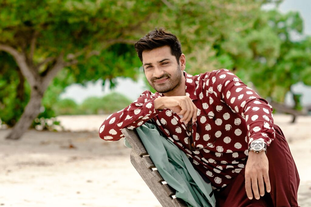 A fashionable man in designer clothing relaxes outdoors on a Maldivian beach.