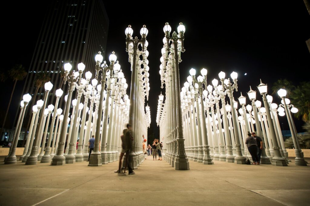 Nighttime view of the Urban Light installation at LACMA with visitors walking between the lit lampposts.