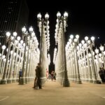 Nighttime view of the Urban Light installation at LACMA with visitors walking between the lit lampposts.