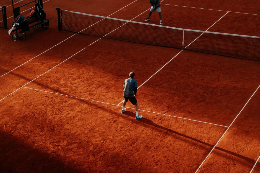 Tennis players competing on a sunlit red clay court in Buenos Aires.