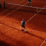 Tennis players competing on a sunlit red clay court in Buenos Aires.