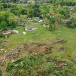 Drone view of uprooted trees heaped on green meadow in small village after massive storm