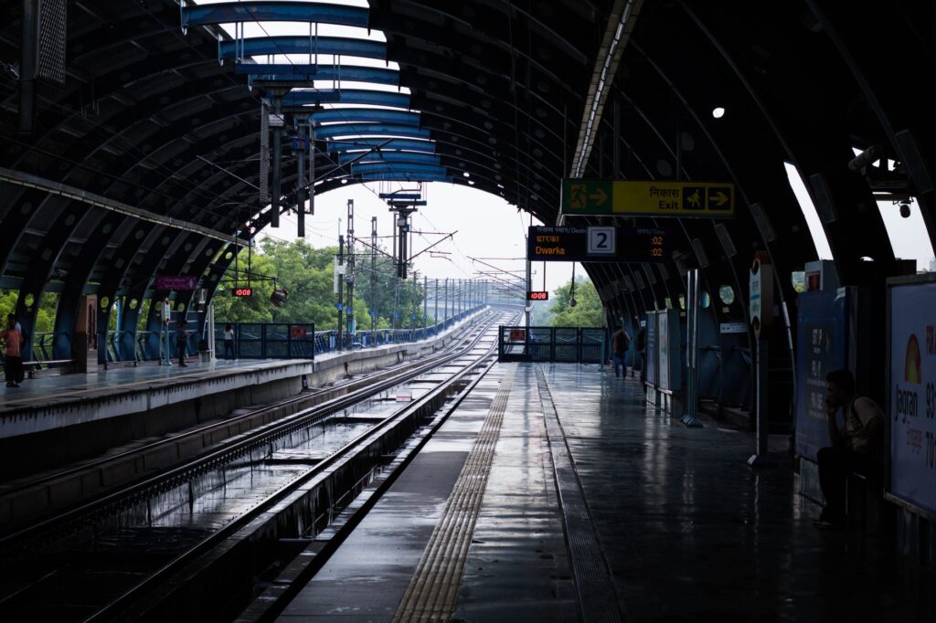 A quiet afternoon at a New Delhi metro station with wet tracks post rain, reflecting urban life.