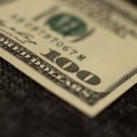 Detailed close-up of a hundred dollar bill resting on dark fabric surface, showcasing texture.