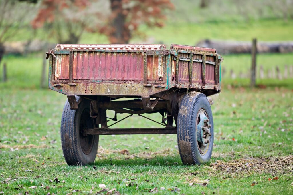A weathered, rusty farm trailer sits abandoned in a lush green field, reflecting rural decay and nostalgia.