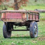 A weathered, rusty farm trailer sits abandoned in a lush green field, reflecting rural decay and nostalgia.