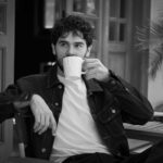 Relaxed black and white portrait of a man enjoying coffee outdoors.