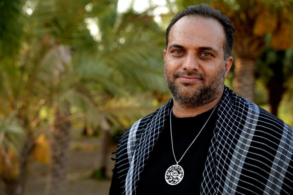 A serene portrait of a man wearing traditional attire in a palm grove in Karbala, Iraq.