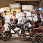 Rickshaw drivers taking a break in the bustling market of Delhi, India, surrounded by goods and vibrant street life.
