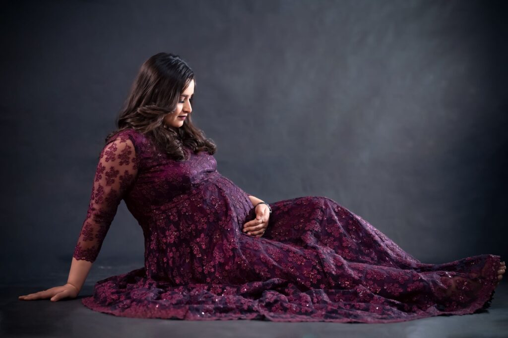 Studio portrait of a pregnant woman in a long, embroidered purple gown, exuding elegance and warmth.