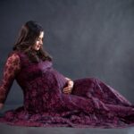 Studio portrait of a pregnant woman in a long, embroidered purple gown, exuding elegance and warmth.
