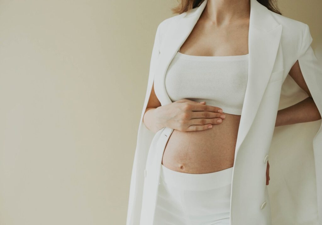 Close-up of a pregnant woman in fashionable attire posing in a studio setting.