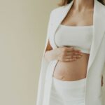 Close-up of a pregnant woman in fashionable attire posing in a studio setting.