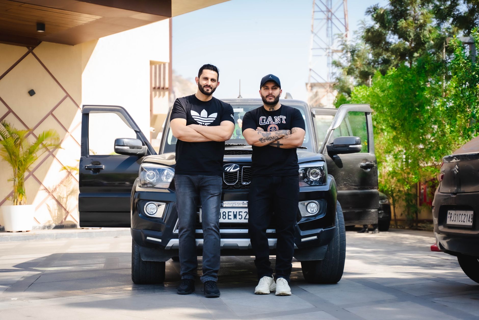 Two men with crossed arms standing in front of an SUV in urban Jaipur, Rajasthan.