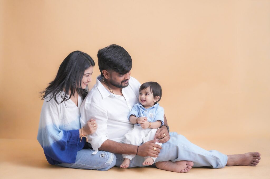 A joyful family portrait featuring parents with their smiling baby in a cozy indoor setting.