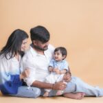 A joyful family portrait featuring parents with their smiling baby in a cozy indoor setting.