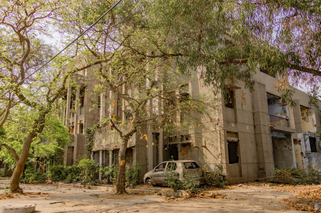An abandoned building surrounded by lush greenery and an old car, captured in Delhi, India.