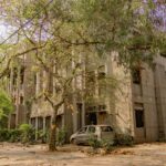 An abandoned building surrounded by lush greenery and an old car, captured in Delhi, India.
