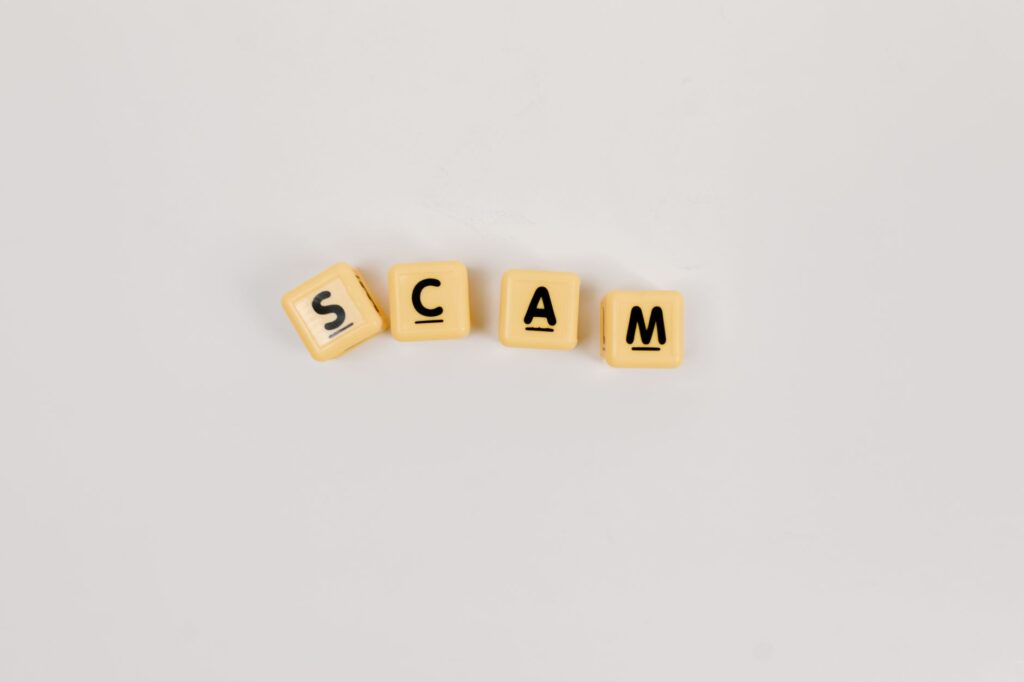 Four Scrabble tiles forming the word 'SCAM' on a neutral background, highlighting concepts like deceit.