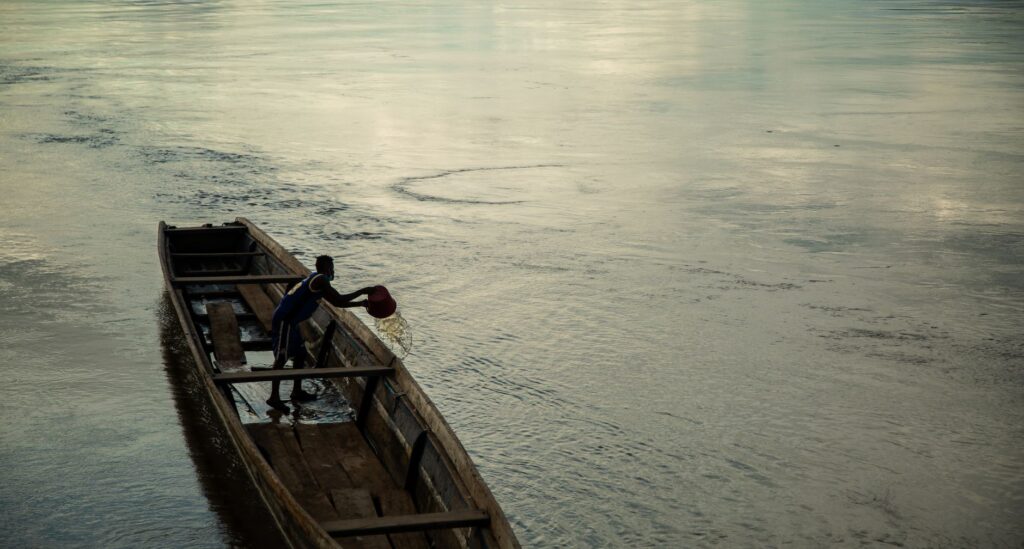 A man bailing water from a canoe on a calm river in Bojayá, Colombia at dusk.