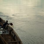 A man bailing water from a canoe on a calm river in Bojayá, Colombia at dusk.