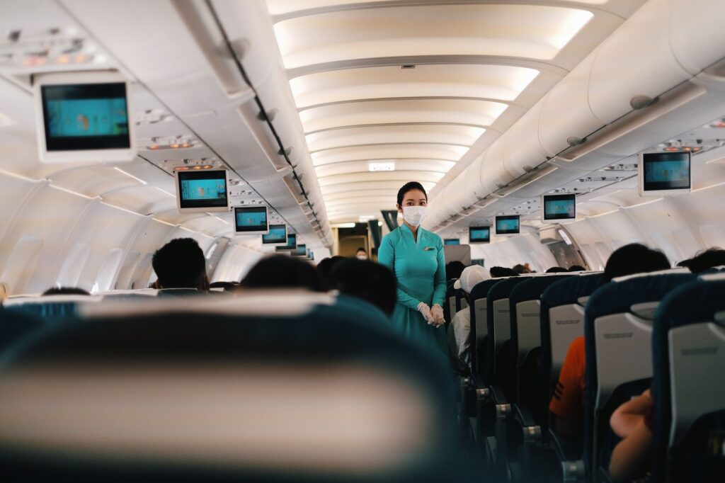 Flight attendant wearing a face mask attending to passengers in an airplane cabin.
