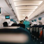 Flight attendant wearing a face mask attending to passengers in an airplane cabin.