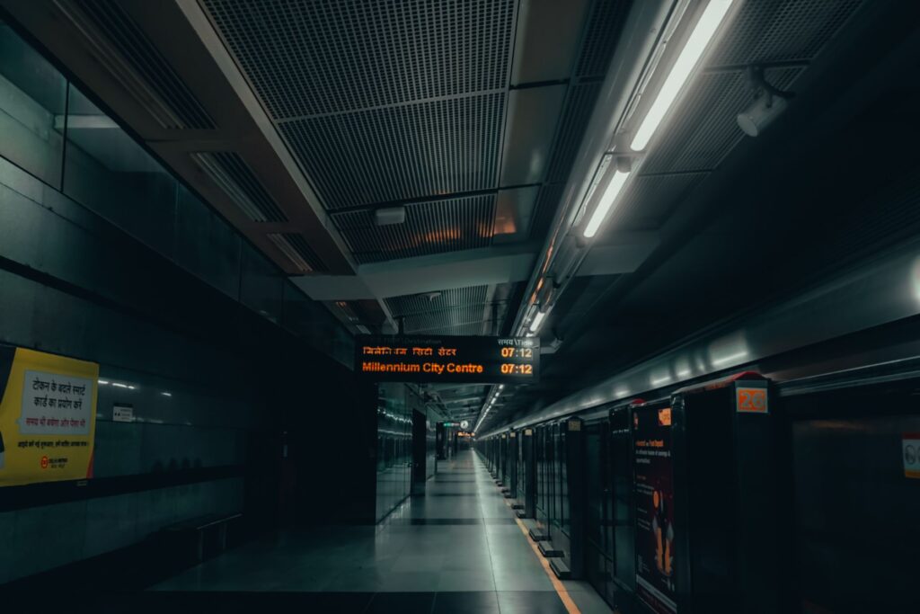 A dimly lit urban subway platform in New Delhi with signs in multiple languages.