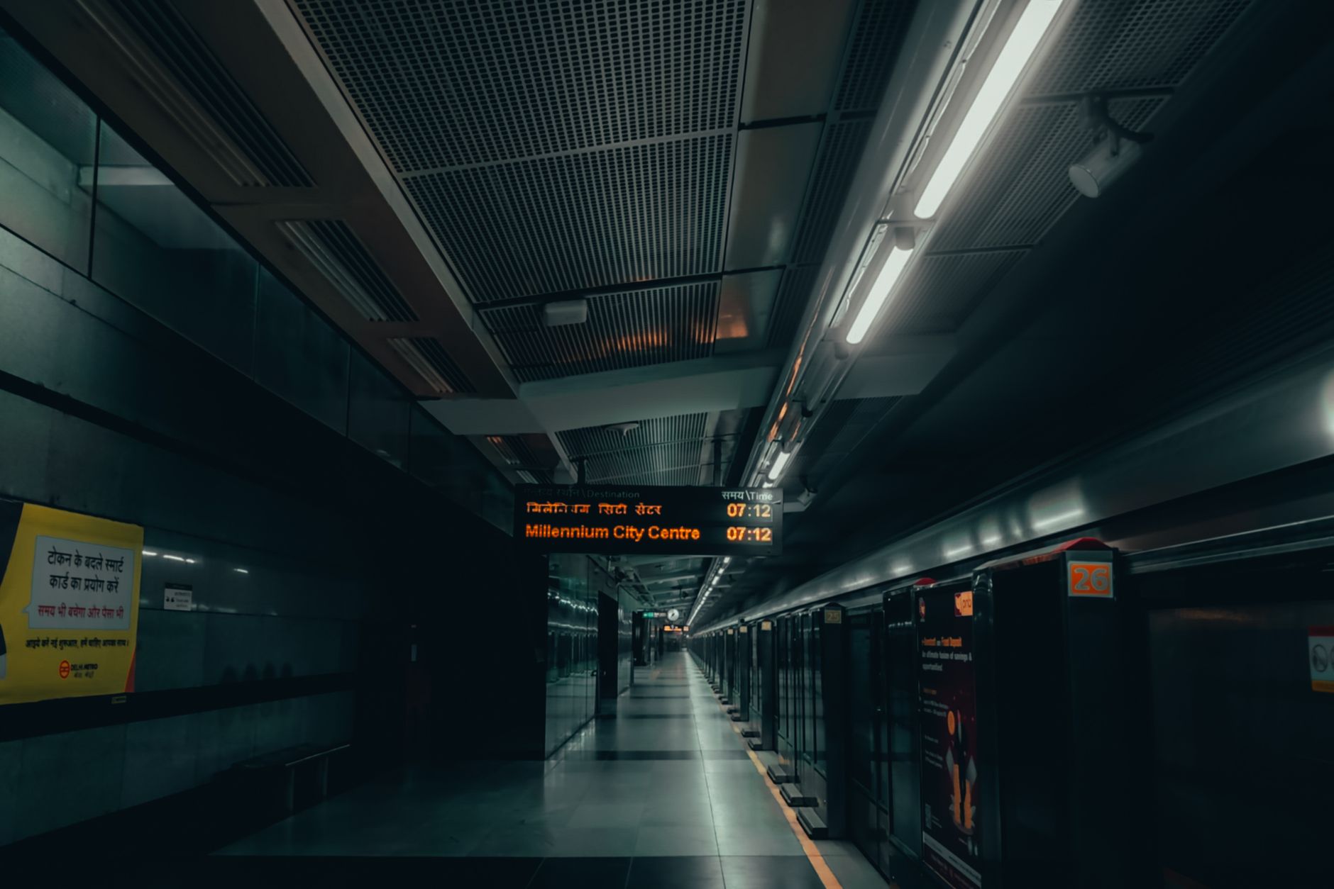 A dimly lit urban subway platform in New Delhi with signs in multiple languages.