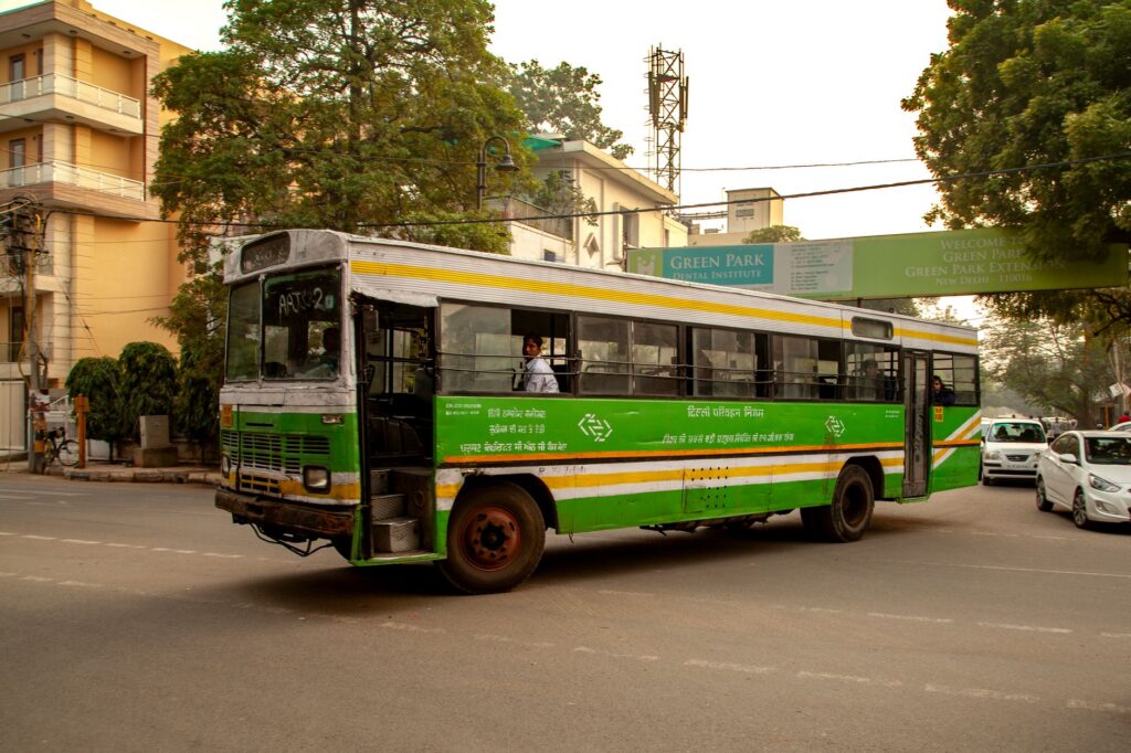A vibrant green public bus navigating through Green Park area in New Delhi, India, during the daytime.