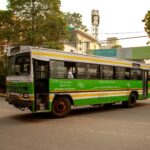 A vibrant green public bus navigating through Green Park area in New Delhi, India, during the daytime.