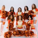 Group of diverse cheerleaders in vibrant uniforms posing with pompoms in a studio setting.