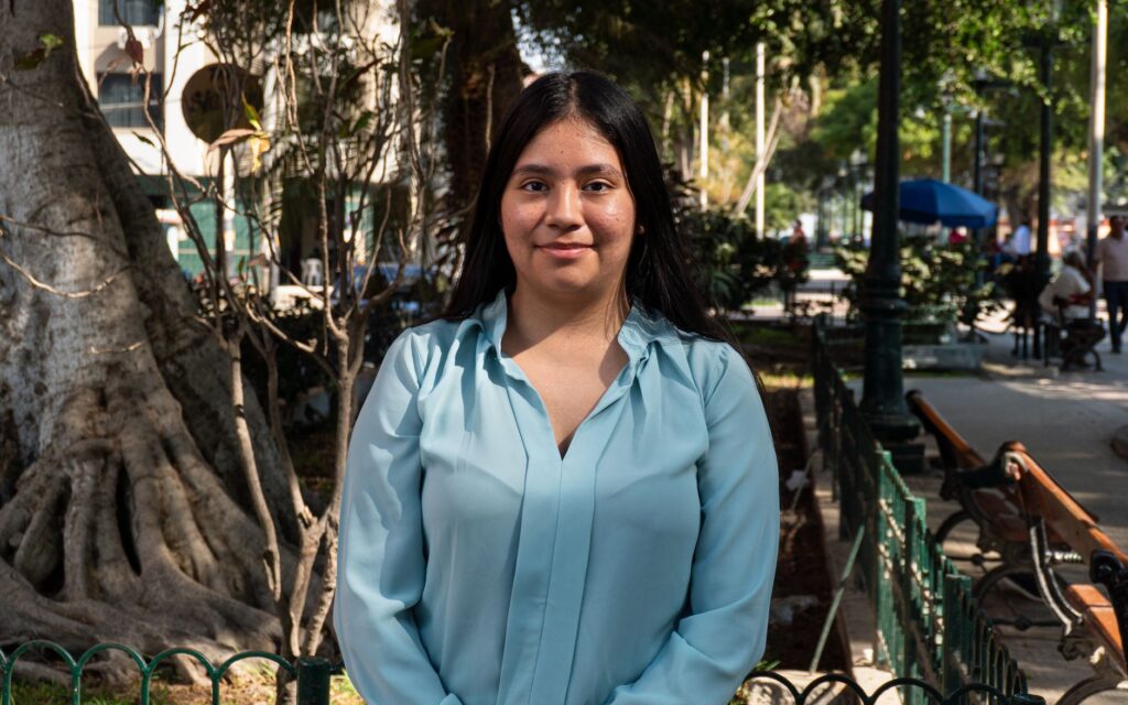 Portrait of a young woman standing in a sunlit park in Piura, Peru.