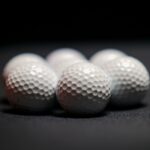 Six white golf balls arranged in close-up on a dark surface, showcasing texture and detail.