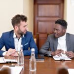 Two businessmen discussing work, seated at a conference table.