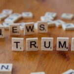 Wooden letter tiles spell 'NEWS' and 'TRUMP' on a wooden table, relating to political discourse.