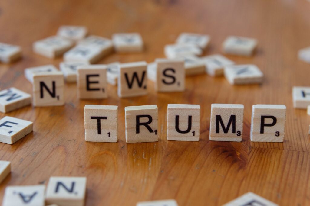Wooden letter tiles spell 'NEWS' and 'TRUMP' on a wooden table, relating to political discourse.