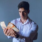A focused adult man counts Argentina pesos indoors, against a neutral backdrop.