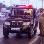 An Indian police officer stands beside a police SUV on a busy roadside in Uttar Pradesh.