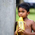 A young boy sips from a yellow tumbler, standing outdoors in Dambulla, Sri Lanka.