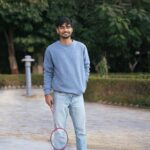 Smiling young man with a badminton racket in a park setting, enjoying leisure time.