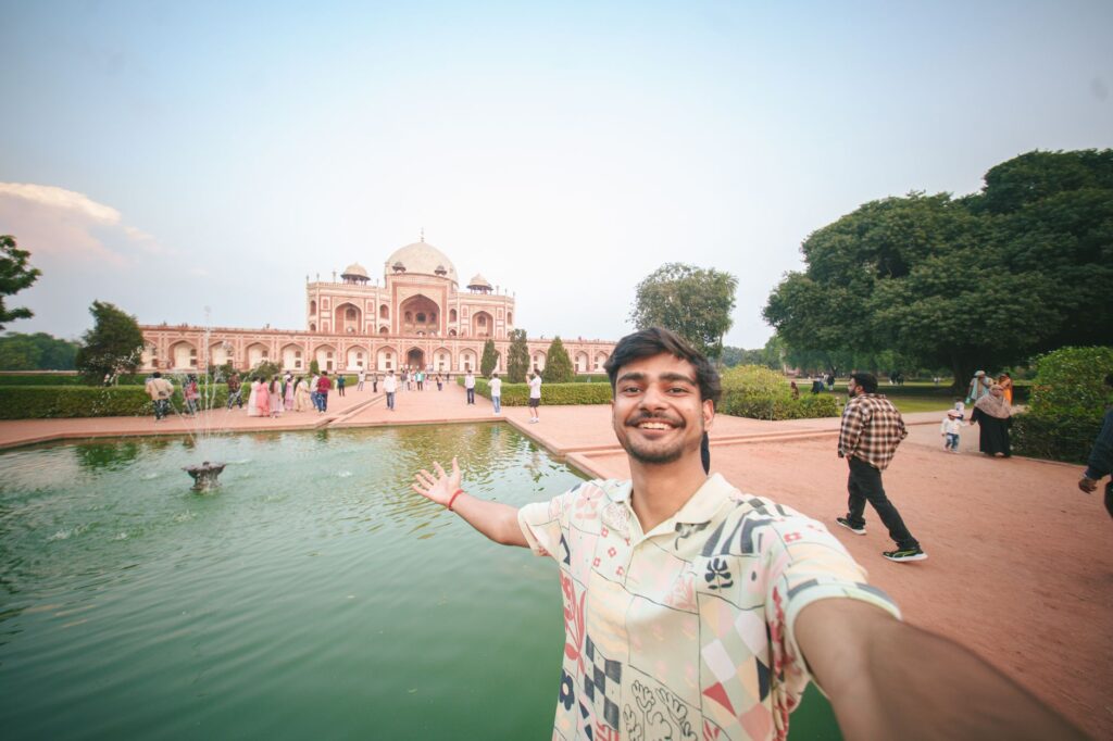 A traveler takes a selfie at Humayun's Tomb in Delhi, showcasing Mughal architecture and a beautiful garden.