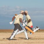 Two cricketers sprint on field, bats in hand, showing dynamic sports action.