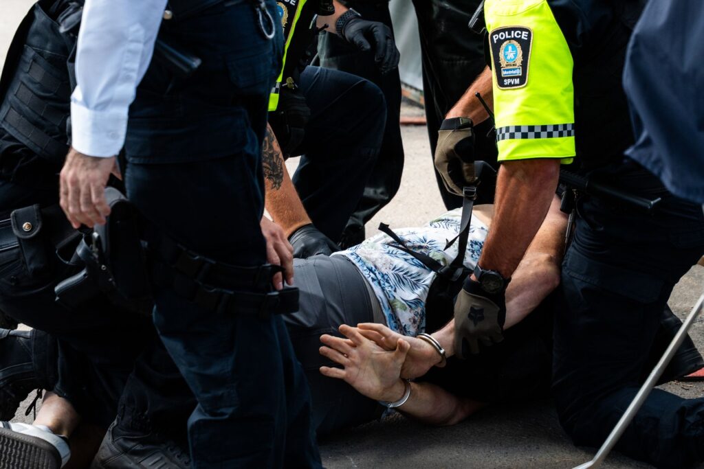 Multiple police officers detain a person on a city street, using handcuffs to restrain them.