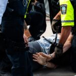 Multiple police officers detain a person on a city street, using handcuffs to restrain them.