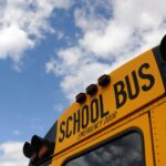 Close-up shot of a yellow school bus with a blue sky background, showcasing cloud formations.