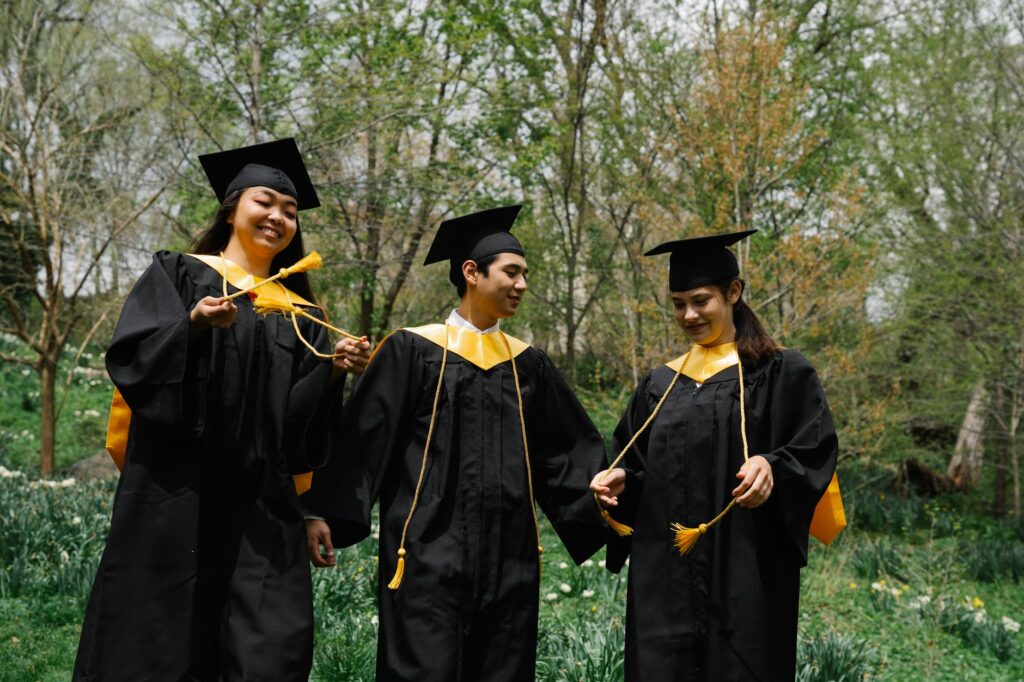Three diverse students celebrate graduation outdoors, sharing joy and accomplishments.