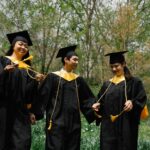 Three diverse students celebrate graduation outdoors, sharing joy and accomplishments.