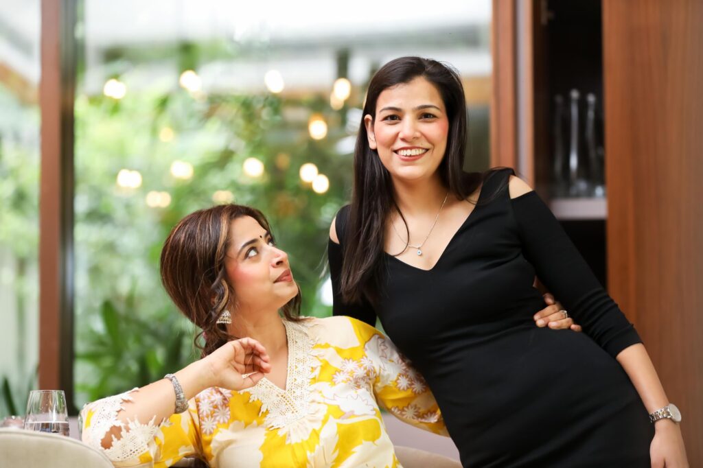 Two smiling women share a light moment indoors, suggesting friendship and joy.