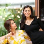 Two smiling women share a light moment indoors, suggesting friendship and joy.